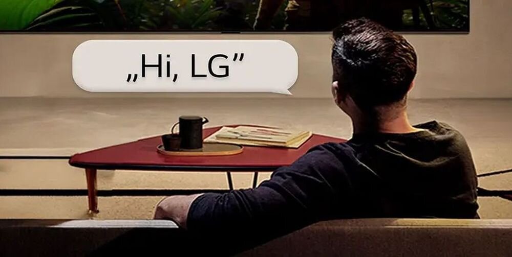 Osoba siedzi na kanapie przed telewizorem, na ekranie widoczny jest tekst: \'Hi, LG\'.