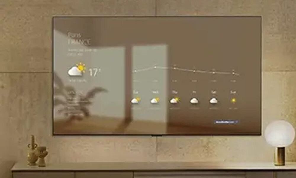 Telewizor wyświetla prognozę pogody dla Paryża z temperaturą 17°C i ikoną słońca za chmurą. Obok telewizora znajduje się lampa i dekoracyjne figurki.