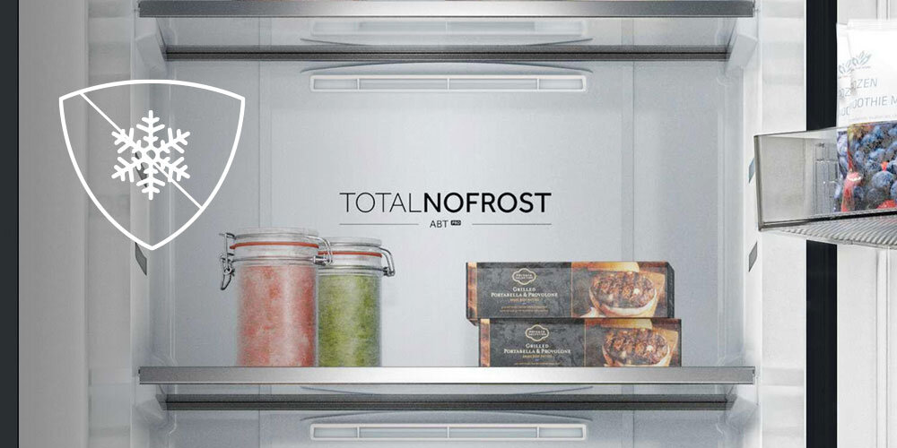 Wnętrze zamrażarki z dwoma półkami, na których znajdują się słoiki z kolorowymi produktami oraz opakowania z jedzeniem. Na tylnej ściance widoczny jest napis \'TOTAL NO FROST\'.