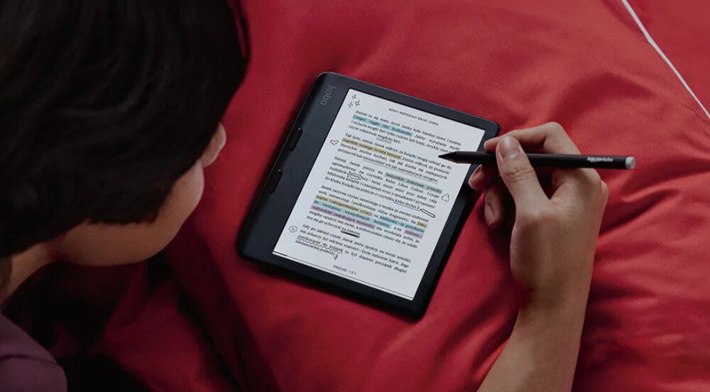 Osoba trzyma czytnik e-booków z wyświetlonym tekstem, który jest podkreślony w różnych kolorach. Obok znajduje się rysik, którym osoba zaznacza tekst na ekranie.