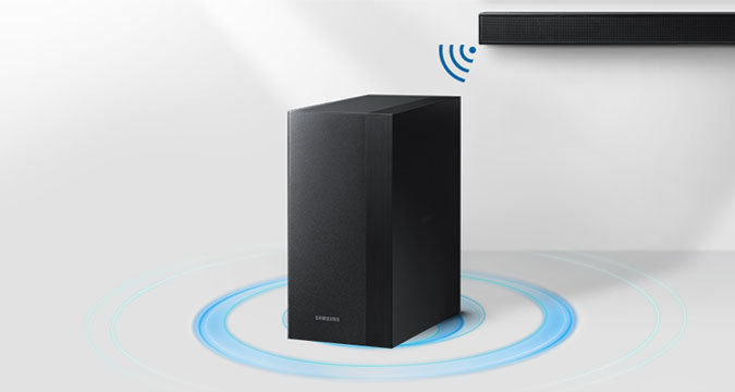 Ilustracja przedstawiająca czarny subwoofer Samsung. Za nim zawieszony jest płaski Soundbar Samsung w kolorze czarnym, który łączy się z subwooferem, co pokazuje ikonka Wi-Fi.