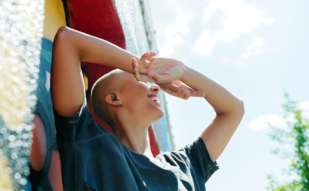 JBL Sense Lite technologia JBL OpenSound czysty dźwięk i otwarty kanał słuchowy, osoba z założonymi słuchawkami leżąca nad wodą