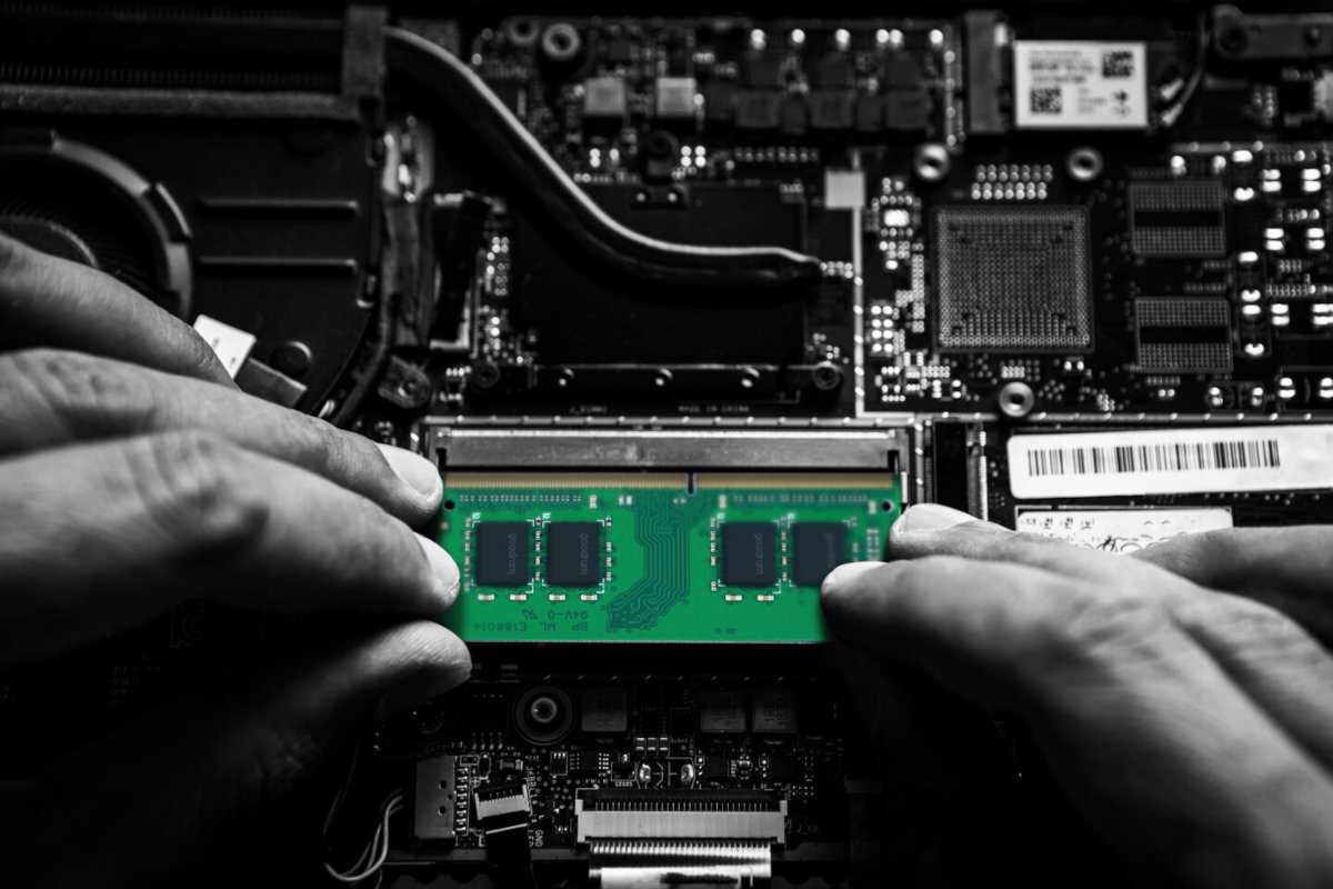 Osoba instaluje zielony moduł pamięci RAM na płycie głównej komputera. W tle widoczne są różne elementy elektroniczne i złącza.