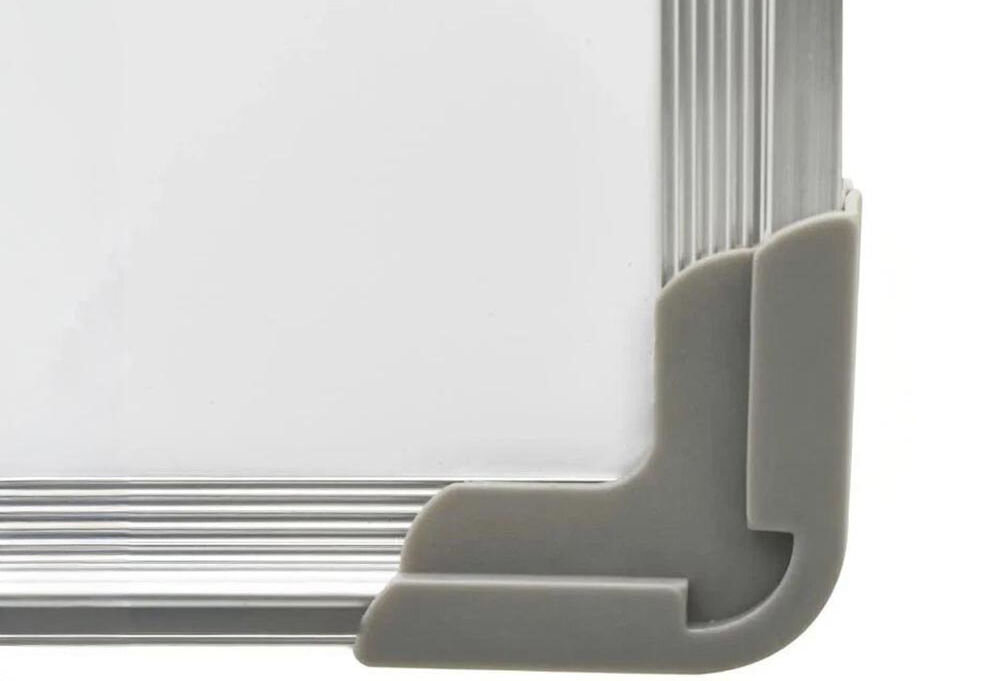 Fragment tablicy magnetycznej z szarym narożnikiem ochronnym i aluminiową ramą. Powierzchnia tablicy jest biała i gładka.