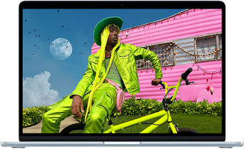 Na ekranie laptopa widać osobę w zielonym stroju siedzącą na żółtym rowerze przed różowym budynkiem. W tle znajduje się niebo z księżycem i chmurami.