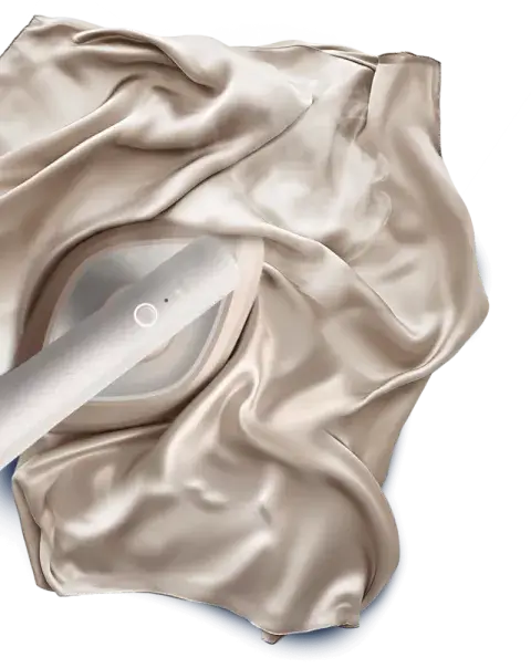 Na obrazie widoczna jest parownica do ubrań w kontakcie z gładką, jasną tkaniną. Parownica ma okrągły przycisk na uchwycie.