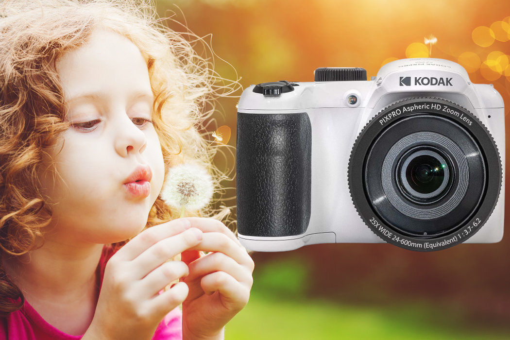 Obraz przedstawia dziecko dmuchające na dmuchawiec oraz biały aparat fotograficzny z logo KODAK. Na obiektywie aparatu widoczny jest napis: \'PIXPRO Aspheric HD Zoom Lens 25X WIDE 24-600mm (Equivalent) 1:3.7-6.2\'.