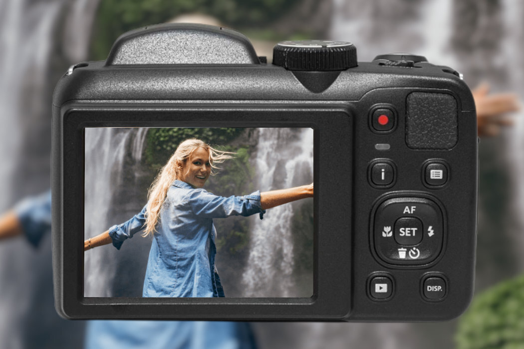 Widok tylnej części aparatu fotograficznego z wyświetlaczem, na którym widać osobę w niebieskiej koszuli na tle wodospadu. Obok ekranu znajdują się przyciski sterujące aparatem.