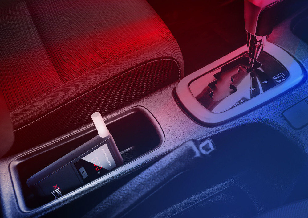 W samochodowym uchwycie na kubki znajduje się alkomat z wyświetlaczem pokazującym wynik 0.00. Obok widoczna jest dźwignia zmiany biegów automatycznej skrzyni biegów.