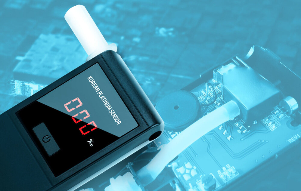 Na obrazie widoczny jest alkomat z wyświetlaczem pokazującym \'0.00%\' oraz napisem \'KOREAN PLATINUM SENSOR\'. W tle znajduje się fragment układu elektronicznego.