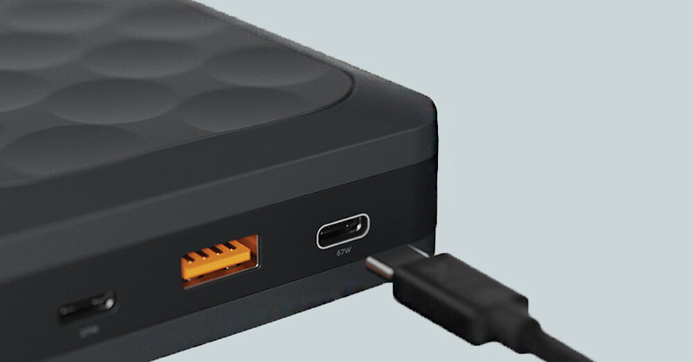 Zbliżenie na czarny powerbank z widocznymi portami USB, w tym jednym oznaczonym jako 67W, oraz podłączonym kablem.