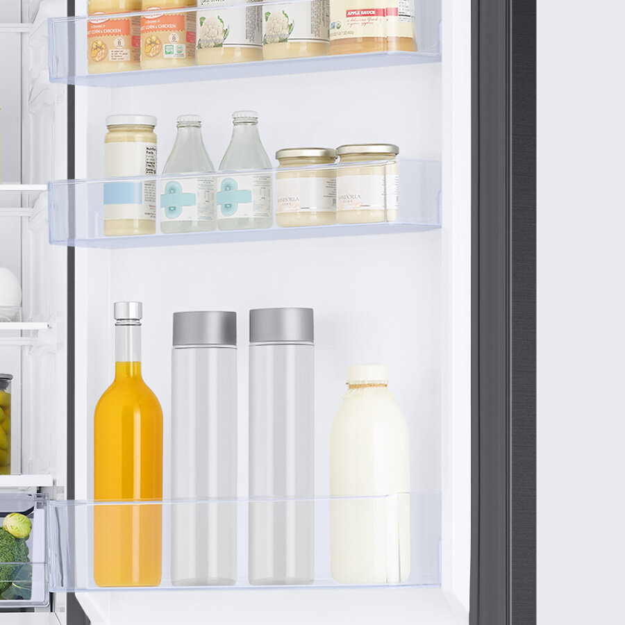 Wnętrze lodówki z widocznymi półkami na drzwiach, na których znajdują się różne produkty spożywcze w słoikach, butelkach i kartonach. Produkty obejmują napoje, słoiki z przetworami oraz kartony z napojami.