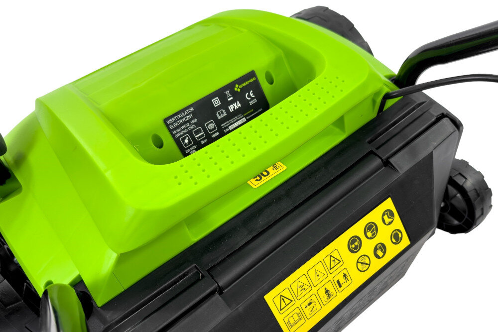Zbliżenie na zielono-czarny wertykulator elektryczny z widocznymi etykietami informacyjnymi i ostrzegawczymi. Na etykiecie widnieje tekst: \'WERTYKULATOR ELEKTRYCZNY GREENSO WE32-1500\'.