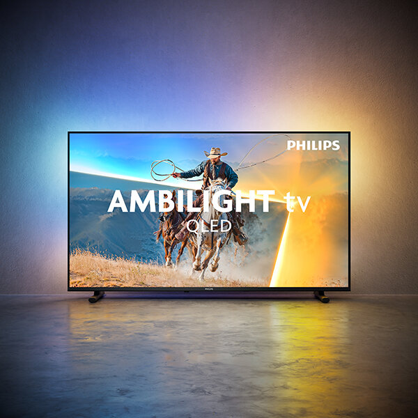 Telewizor wyświetla obraz kowboja na koniu z lasso, z efektem Ambilight na ścianie. Na ekranie widoczny jest tekst: \'PHILIPS AMBILIGHT tv OLED\'.