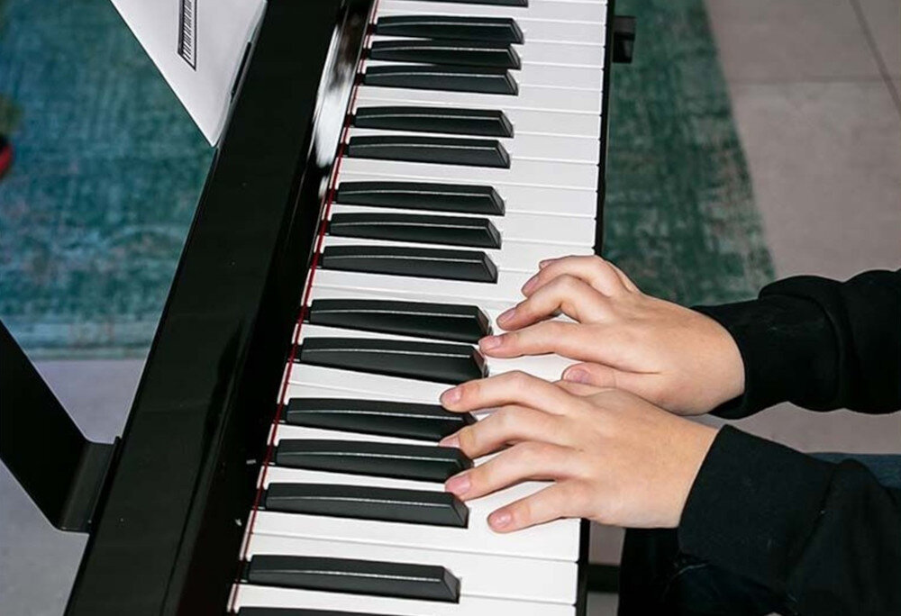 Osoba gra na klawiaturze pianina cyfrowego, widoczne są białe i czarne klawisze oraz dłonie naciskające klawisze.