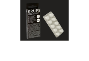 Na obrazie widoczna jest czarna paczka z napisem \'KRUPS\' oraz przezroczysta blistra z białymi tabletkami. Paczka zawiera tekst w języku angielskim i francuskim.