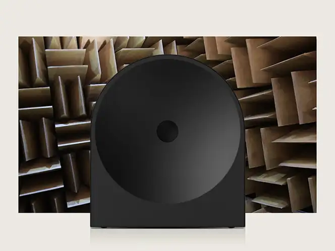 2026-hw-ls50h-samsung-audio-lab-mo 664x498 Czarny głośnik o nowoczesnym designie na tle pomieszczenia z panelami akustycznymi. Panele mają różne odcienie brązu i są ułożone w geometryczny wzór.