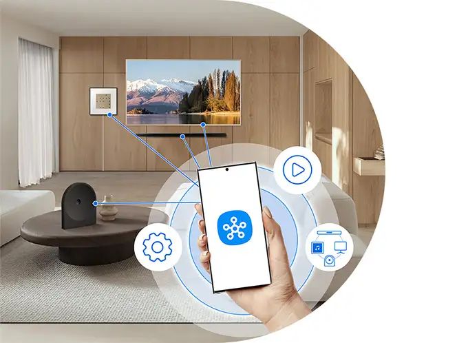 2026-hw-ls50h-smartthings-app 664x498 W nowoczesnym salonie znajduje się telewizor wyświetlający krajobraz górski oraz głośnik na stoliku. Na pierwszym planie widoczny jest smartfon z ikoną aplikacji, otoczony symbolami ustawień, odtwarzania i połączeń.