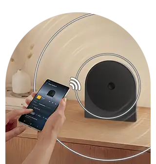 wireless music streaming 320x335 Osoba trzyma smartfon z aplikacją muzyczną, a obok na drewnianej powierzchni stoi czarny głośnik o nowoczesnym designie. W tle widoczna jest dekoracyjna roślina i okrągłe linie symbolizujące połączenie bezprzewodowe.