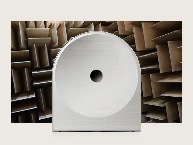 2026-hw-ls51h-samsung-audio-lab-mo 664x498 Biały głośnik o zaokrąglonym kształcie z centralnym otworem, umieszczony na tle pomieszczenia z panelami akustycznymi.