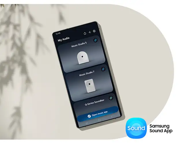 2026-hw-ls51h-samsung-sound-app 664x498 Na obrazie widoczny jest smartfon z aplikacją \'My Audio\', pokazującą listę urządzeń: Music Studio 5, Music Studio 7 i Q-Series Soundbar. W prawym dolnym rogu znajduje się logo \'Sound Samsung Sound App\'.