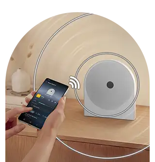 wireless music streaming-ls51h 320x335 Na drewnianej powierzchni stoi biały głośnik o okrągłym kształcie. Obok osoba trzyma smartfon z aplikacją do sterowania muzyką.