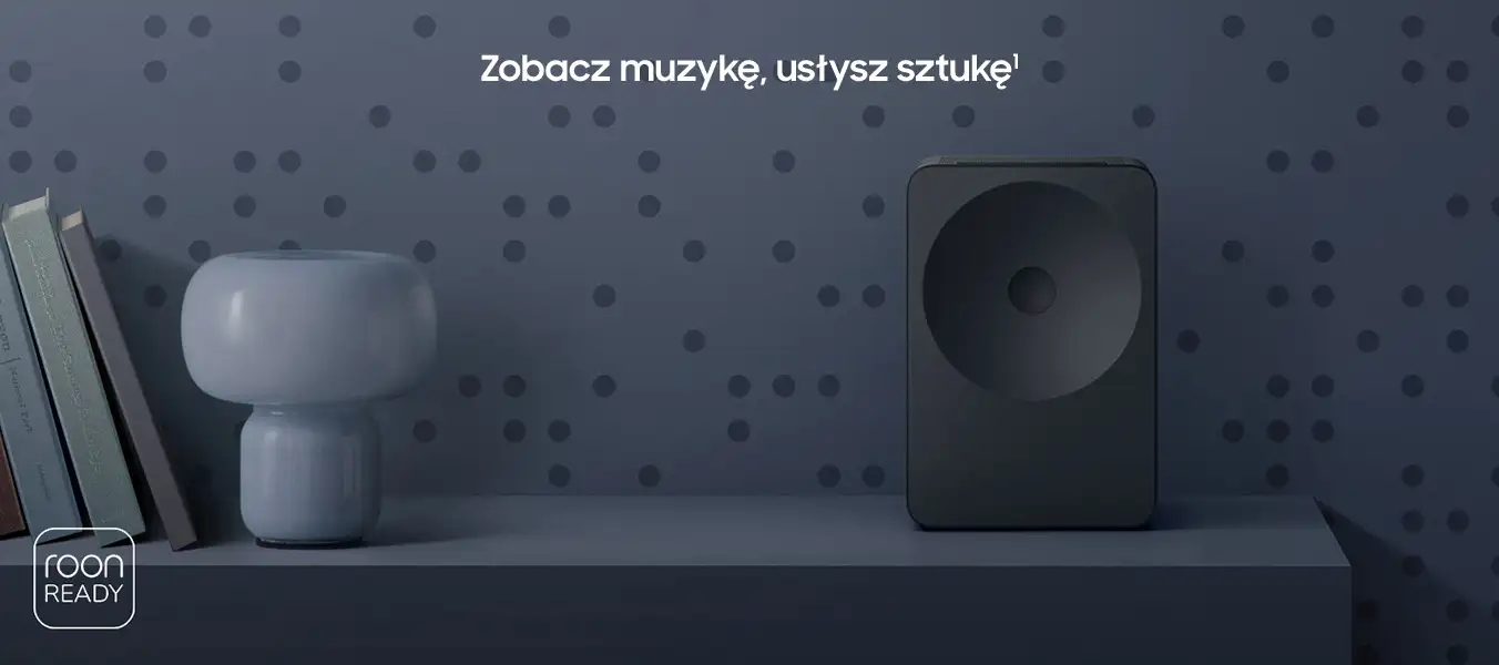 2026-hw-ls70h-kv-pc 1352x600 Na półce znajduje się czarny głośnik oraz lampa obok kilku książek. Na ścianie widoczny jest napis \'Zobacz muzykę, usłysz sztukę\' oraz logo \'roon ready\'.
