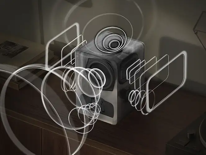 2026-hw-ls70h-top-4-true-311ch-immersive-sound-mo 664x498 Na obrazie widoczny jest czarny głośnik z efektami graficznymi przedstawiającymi fale dźwiękowe wokół niego. Głośnik stoi na drewnianej powierzchni, a w tle znajdują się książki.