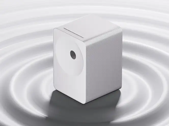 2026-hw-ls71h-ai-dynamic-bass-control-mo 664x498 Biały głośnik o prostokątnym kształcie z widocznym okrągłym elementem na przedniej części, umieszczony na powierzchni z koncentrycznymi falami.