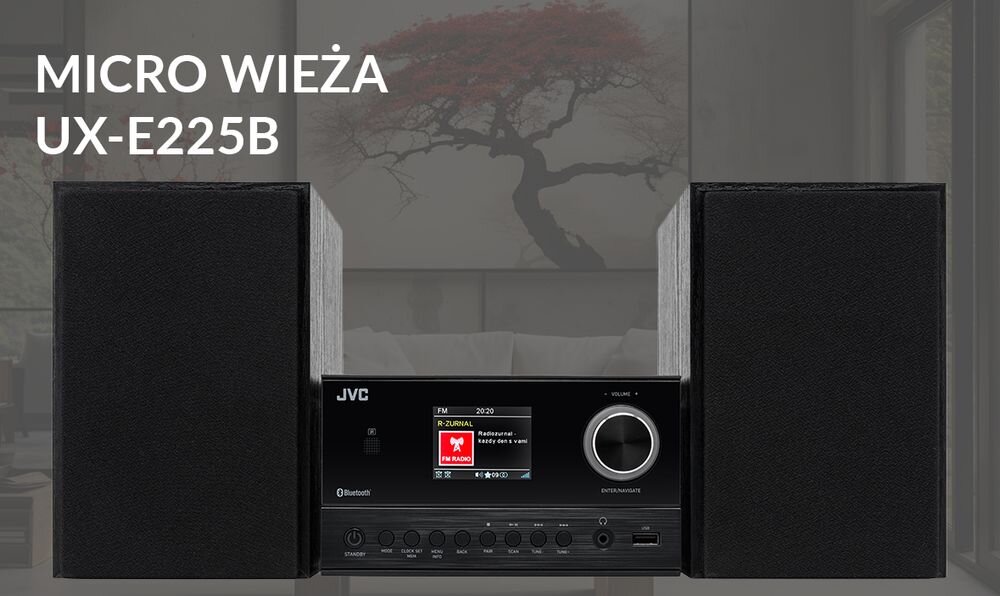 Na obrazie widoczna jest czarna mikro wieża JVC UX-E225B z dwoma głośnikami po bokach. Na wyświetlaczu LCD znajduje się informacja o odtwarzanej stacji radiowej, a obok widoczny jest duży pokrętło regulacji głośności.