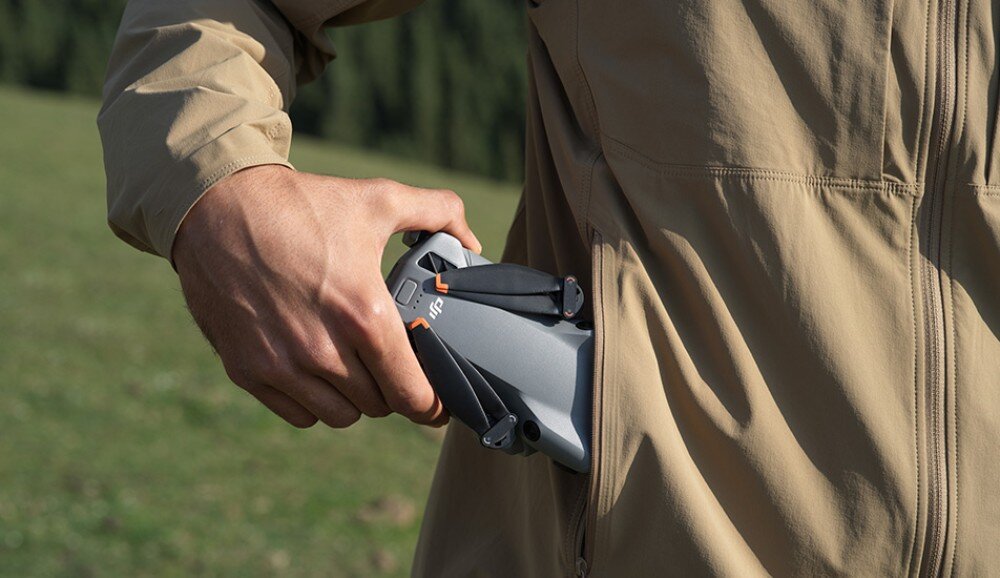 Osoba wkłada szary dron z logo DJI do kieszeni kurtki w plenerze.