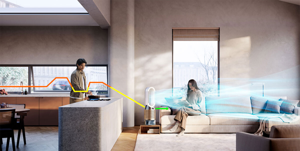 W nowoczesnym wnętrzu znajduje się oczyszczacz powietrza z wentylatorem, z którego wydobywa się strumień powietrza. W tle widać osobę siedzącą na kanapie oraz osobę stojącą przy blacie kuchennym.