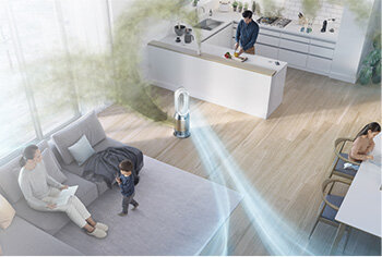 W przestronnym salonie z aneksem kuchennym znajduje się oczyszczacz powietrza, z którego wydobywają się strumienie powietrza. W pomieszczeniu przebywają trzy osoby, a w tle widać kuchnię z wyspą.