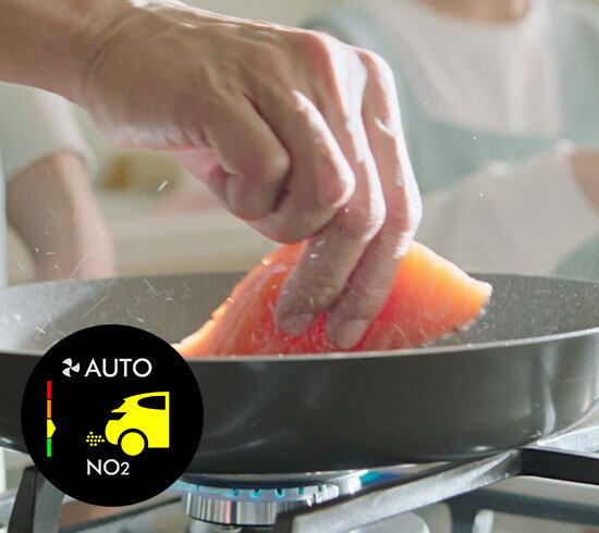 Osoba trzyma kawałek łososia nad patelnią na kuchence gazowej. W lewym dolnym rogu widoczna jest ikona z napisem \'AUTO NO2\' i symbolem samochodu.