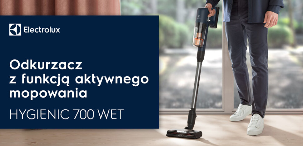 Osoba trzyma odkurzacz pionowy w jasnym pomieszczeniu. Obok widoczna jest tablica z logo Electrolux i tekstem: \'Odkurzacz z funkcją aktywnego mopowania HYGIENIC 700 WET\'.