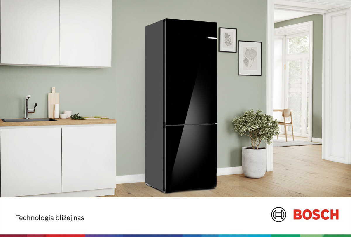 Czarna lodówka stoi w nowoczesnej kuchni z jasnymi ścianami i drewnianą podłogą. Na dole widoczne jest logo BOSCH oraz tekst \'Technologia bliżej nas\'.