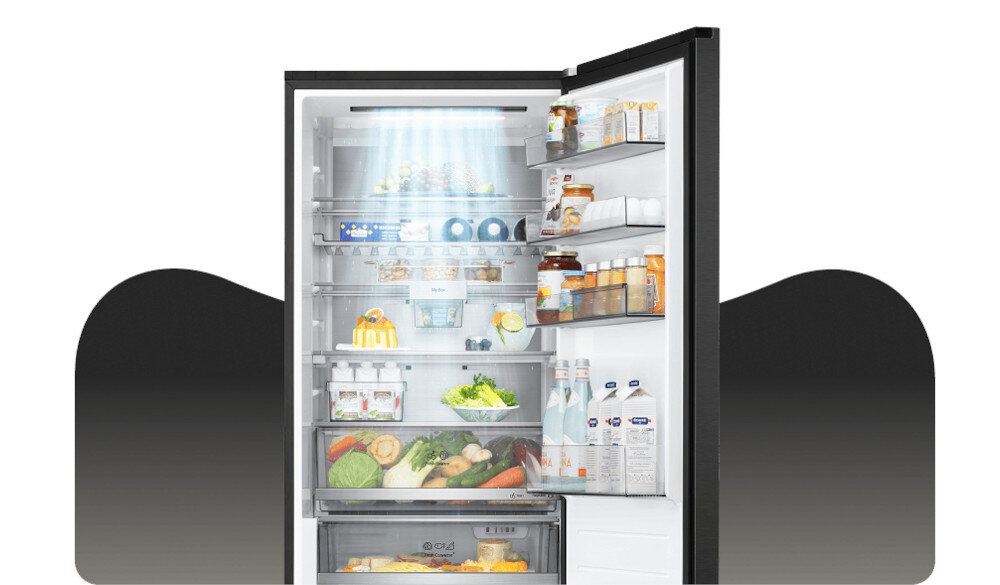 Otwarta lodówka wypełniona różnorodnymi produktami spożywczymi, takimi jak warzywa, owoce, napoje i słoiki. Wnętrze jest jasno oświetlone, a na drzwiach znajdują się dodatkowe półki z produktami.