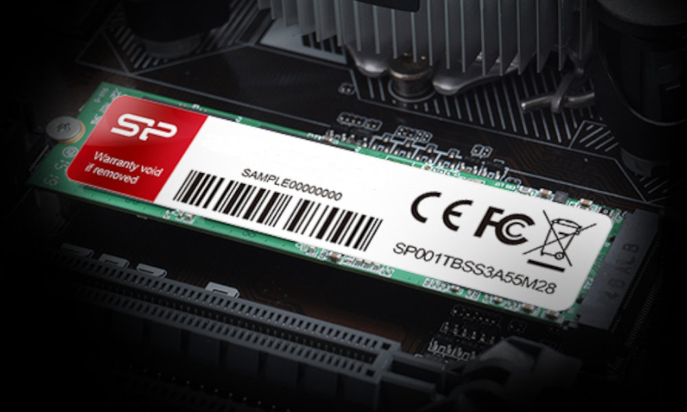 Na obrazie widoczny jest dysk SSD z etykietą zawierającą logo SP, kod kreskowy oraz oznaczenia CE i FCC. Etykieta zawiera również tekst: \'Warranty void if removed\' oraz \'SAMPLE00000000\'.