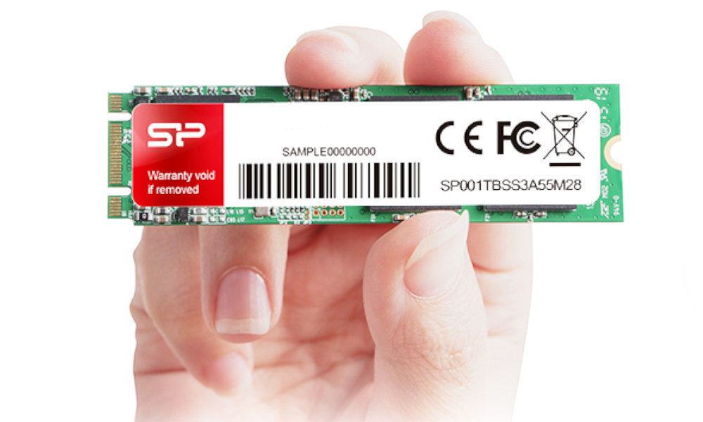Osoba trzyma dysk SSD z widocznym logo SP i etykietą zawierającą tekst: \'Warranty void if removed\', \'SAMPLE00000000\', \'SP001TBSS3A55M28\'.
