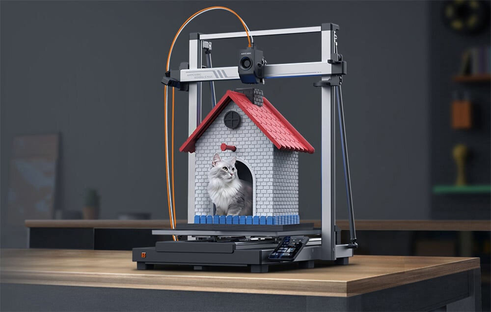 Drukarka 3D ANYCUBIC Kobra 3 Max Combo Wi-Fi, LAN + Dysza + Filament PLA Czarny Duża drukarka 3D Anycubic Kobra 3 Max z wydrukowanym modelem domku dla kota, w którym siedzi prawdziwy, szaro-biały puszysty kot drukarka 3D inteligentne funkcje wsparcie skomplikowanych zadań profesjonaliści hobbyści wariant combo płynne drukowanie wiele kolorów do 8 jednocześnie