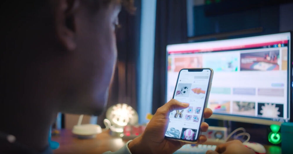 Drukarka 3D ANYCUBIC Kobra 3 Max Combo Wi-Fi, LAN + Dysza + Filament PLA Czarny Osoba trzymająca smartfon z uruchomioną aplikacją mobilną do przeglądania i wybierania modeli 3D do druku, z monitorem komputera w tle kompatybilna ze slicerem Anycubic Slicer Next dedykowana aplikacja Anycubic APP zdalna obsługa LAN Wi-Fi