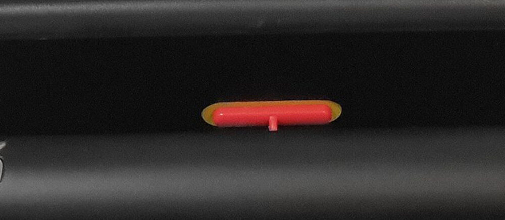 Obraz przedstawia czarną powierzchnię z małym, czerwonym elementem w kształcie prostokąta z zaokrąglonymi krawędziami, umieszczonym na żółtym tle.