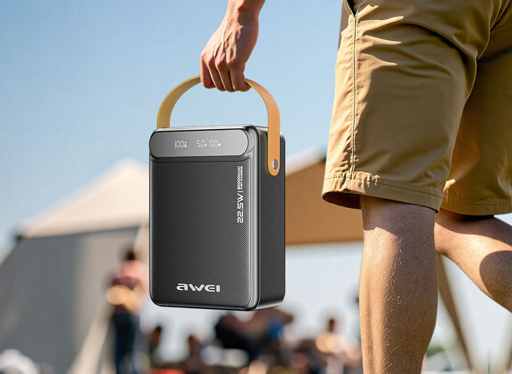 Osoba trzyma czarny powerbank z uchwytem, na którym widnieje napis \'22.5W PD\'. W tle widać rozmyte postacie i namiot.