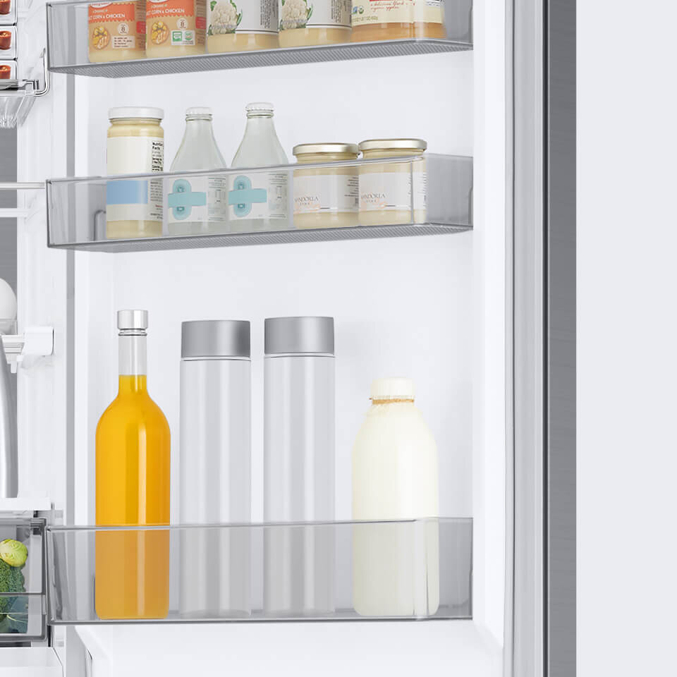 Wnętrze lodówki z trzema półkami na drzwiach, na których znajdują się różne produkty spożywcze, w tym butelki i słoiki. Półki są wykonane z przezroczystego materiału, a lodówka ma wykończenie ze szczotkowanej stali nierdzewnej.