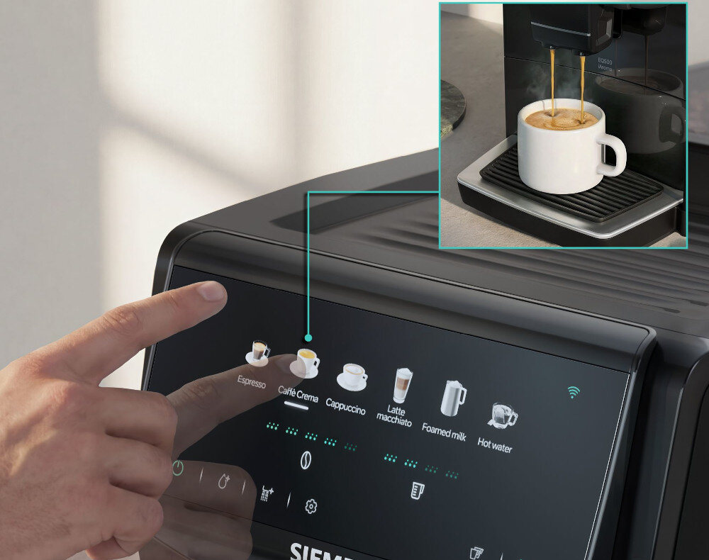 Osoba dotyka panelu dotykowego ekspresu do kawy, na którym widoczne są ikony różnych napojów, takich jak Espresso, Caffè Crema, Cappuccino, Latte macchiato, Foamed milk i Hot water. W górnym rogu znajduje się zbliżenie na filiżankę kawy pod dyszą ekspresu.