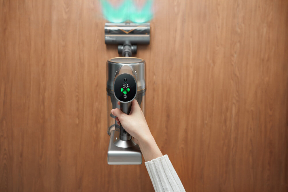 Osoba trzyma odkurzacz z wyświetlaczem pokazującym 80% i ikoną baterii. Odkurzacz jest używany na drewnianej podłodze.