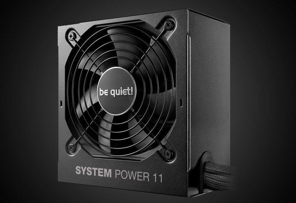 Na obrazie widoczny jest czarny zasilacz komputerowy z wentylatorem, na którym znajduje się napis \'be quiet!\'. Na obudowie zasilacza widnieje tekst \'SYSTEM POWER 11\'.