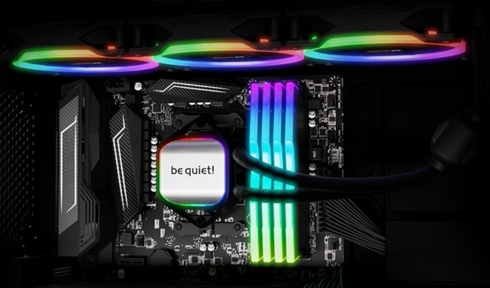 Komputer MAD DOG BQ900FX-A04DR32 Wnętrze obudowy komputera z widoczną płytą główną oraz systemem chłodzenia wodnego procesora, na którego bloku widnieje biały napis 'be quiet!'. Nad podzespołami znajdują się trzy wentylatory z pierścieniami RGB świecącymi w kolorach tęczy, chłodzenie procesora, podświetlenie, wentylatory