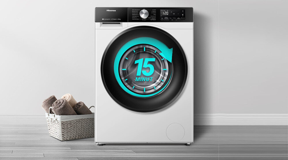 Pralka z wyświetlaczem pokazującym napis \'15 MINUT\' w centralnej części drzwi. Obok znajduje się kosz z ręcznikami na drewnianej podłodze.