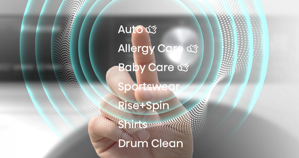 Obraz przedstawia dłoń wskazującą na przezroczysty interfejs z listą programów pralki: Auto, Allergy Care, Baby Care, Sportswear, Rise+Spin, Shirts, Drum Clean. W tle widoczne są koncentryczne kręgi świetlne.